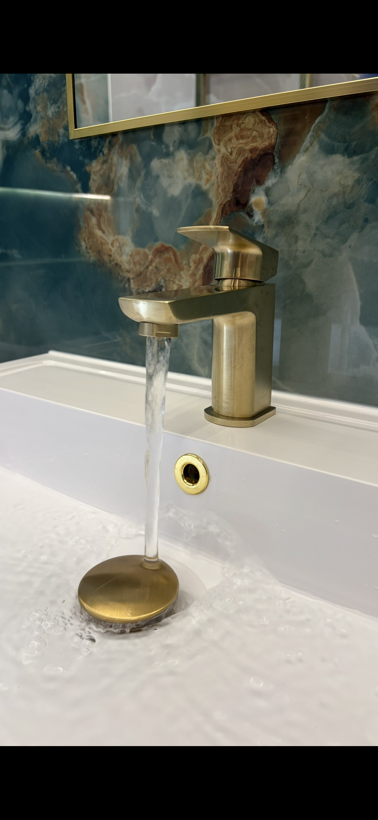 Brushed brass basin tap running water against green marble feature wall