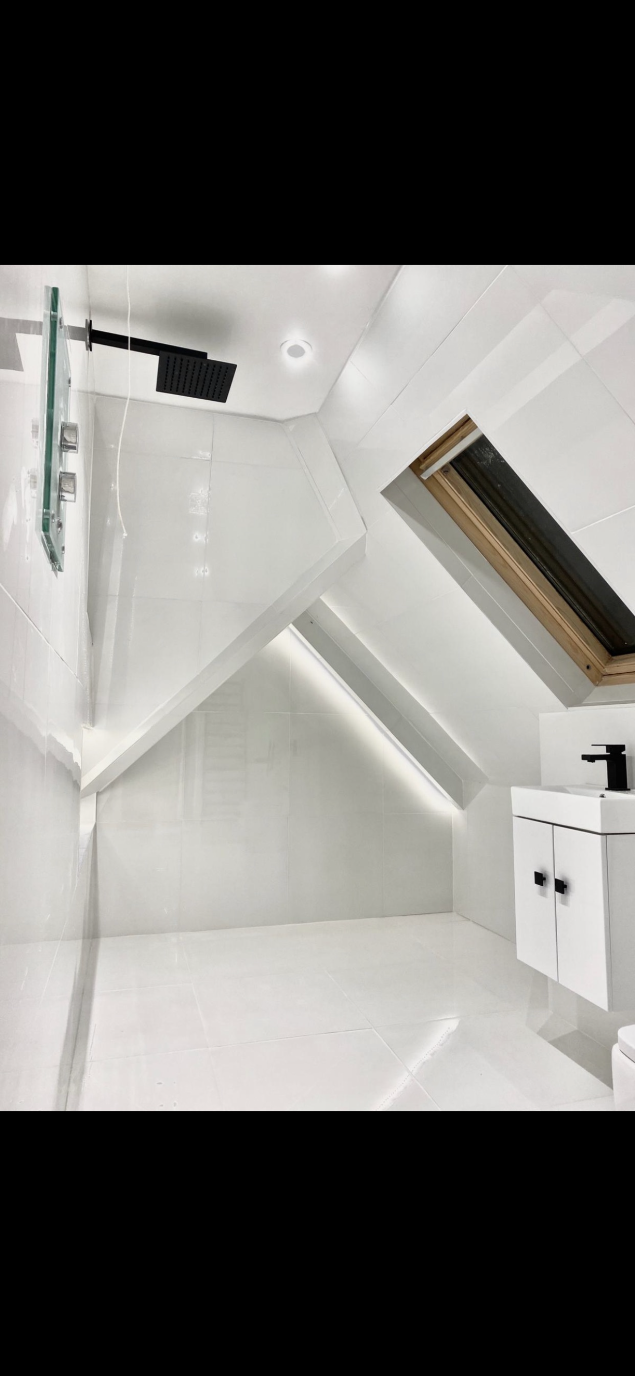 Bright white attic bathroom with walk-in shower, skylight and black fixtures