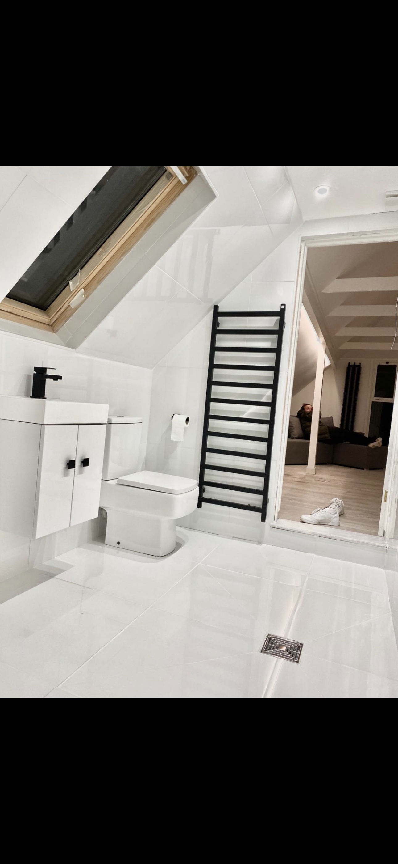 White attic bathroom with skylight, black towel rail and large format floor tiles