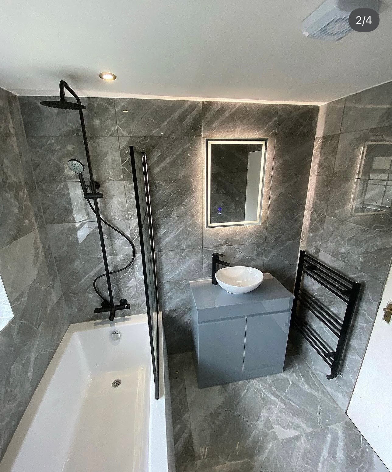 Grey marble bathroom overview with black rain shower, vanity unit and heated towel rail