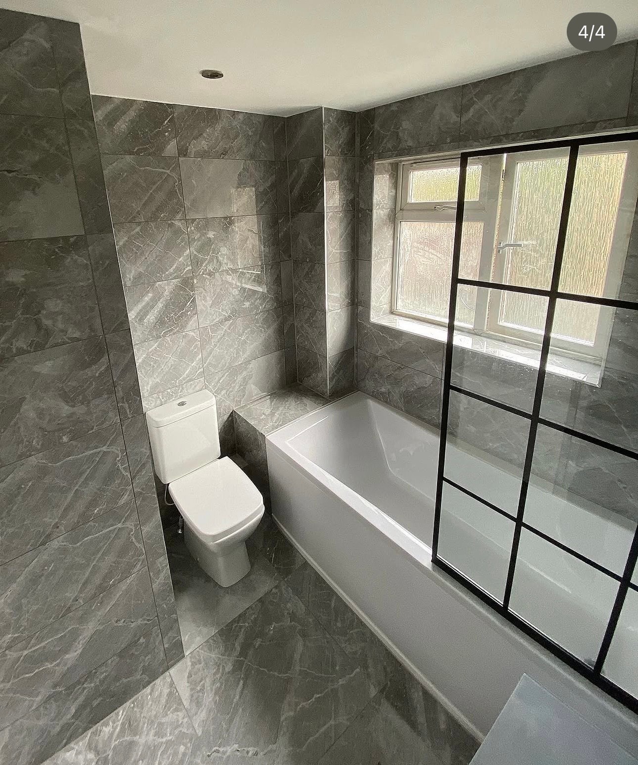 Grey marble bathroom with bath, black grid screen and WC