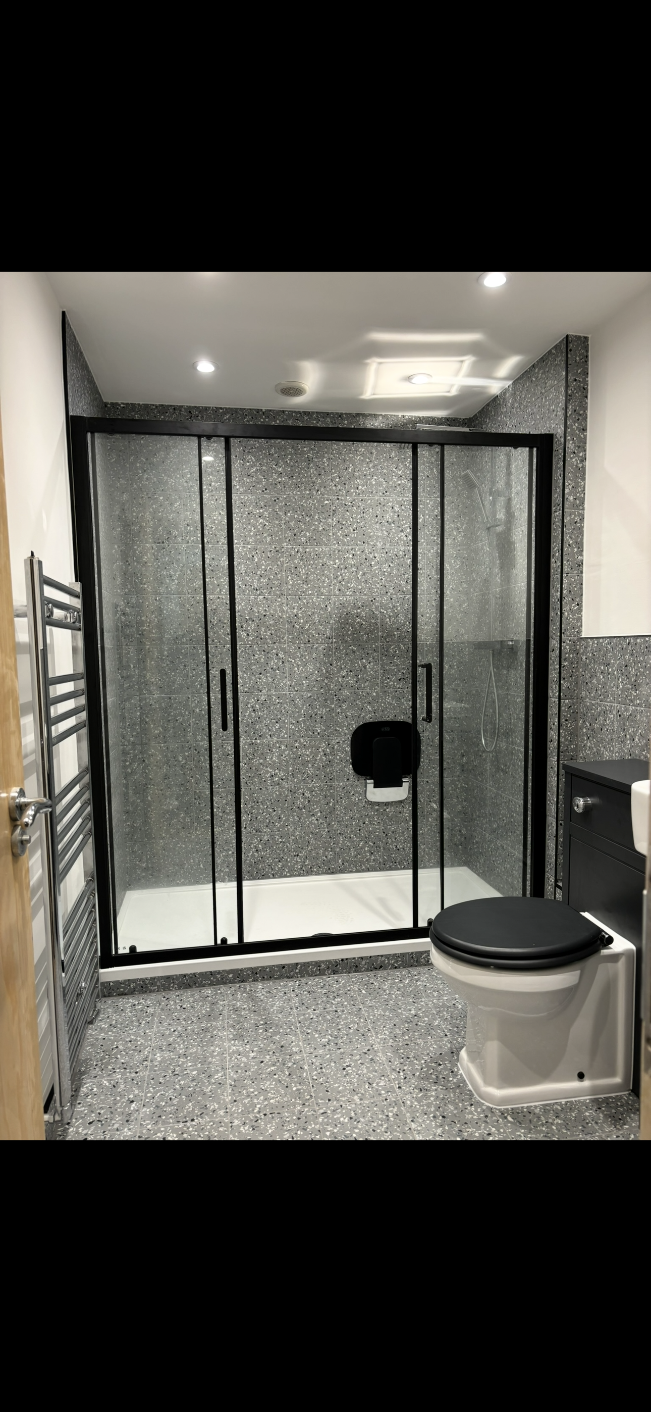 Terrazzo tiled bathroom with large black-framed sliding shower enclosure and black WC