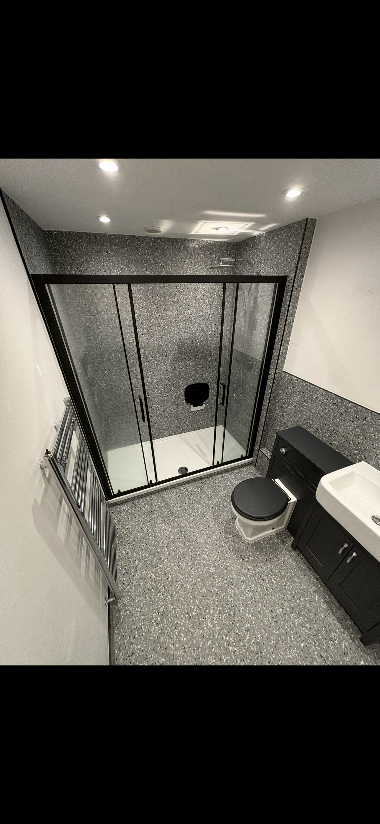 Terrazzo tiled bathroom overhead view with black sliding shower enclosure and dark vanity