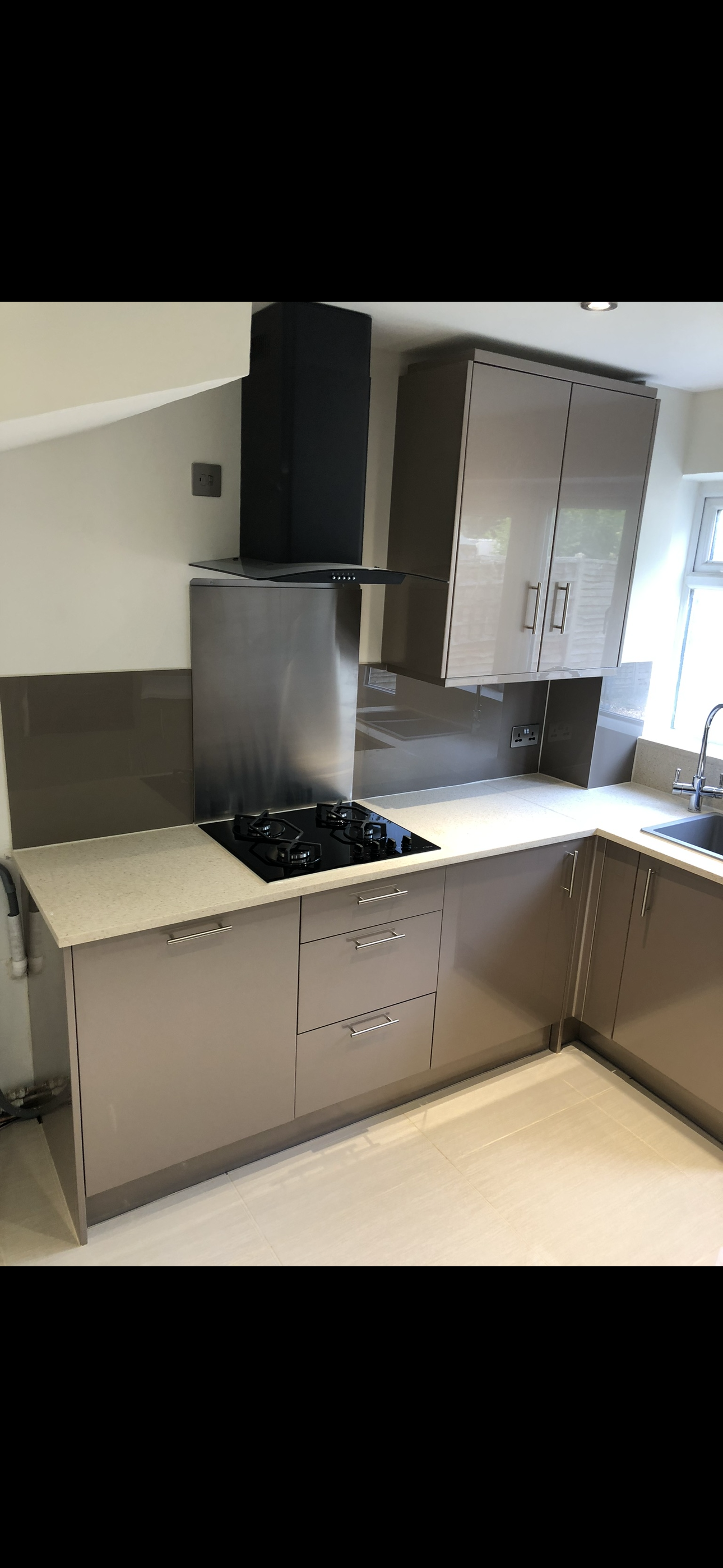Grey gloss kitchen with black gas hob, stainless steel splashback and black extractor fan