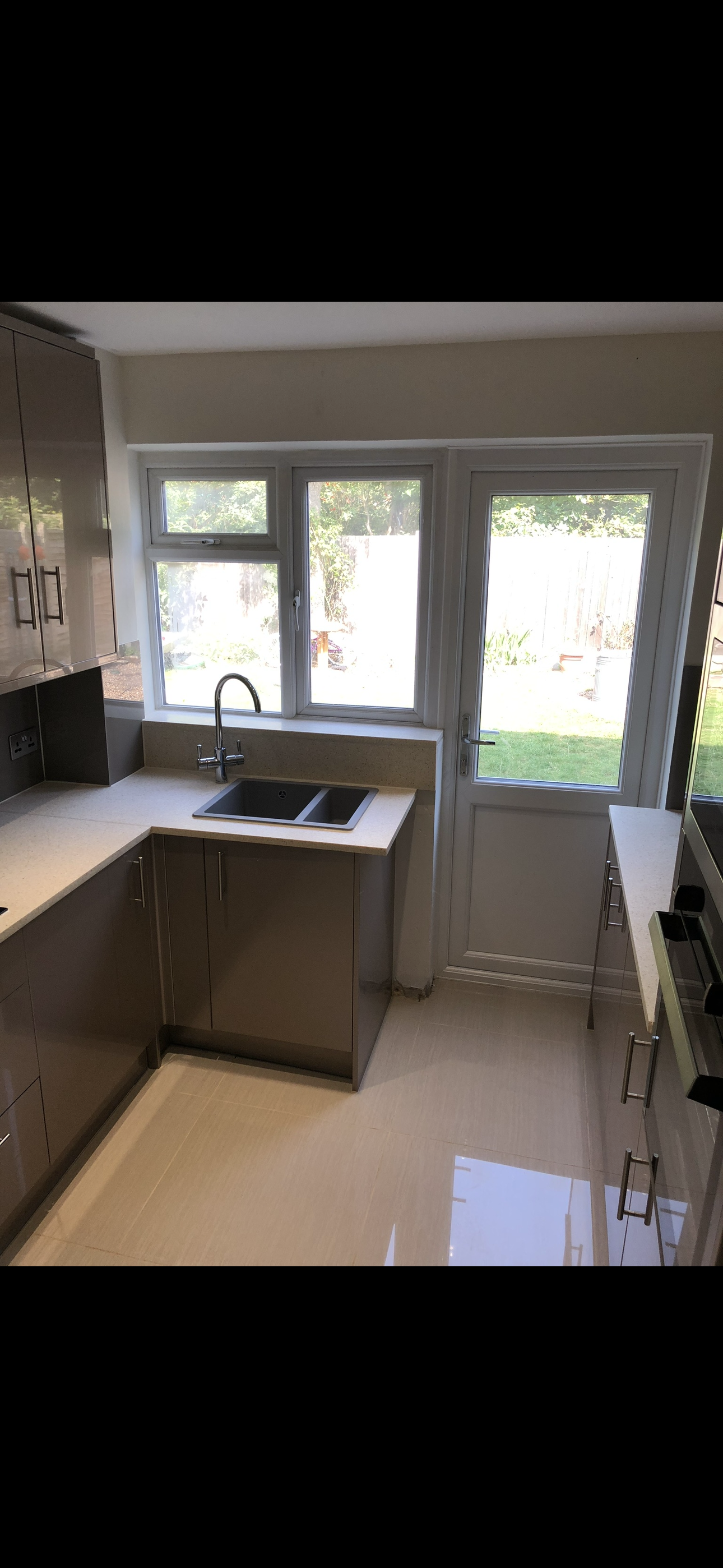 Grey gloss kitchen with undermount sink, garden-view window and white quartz worktops