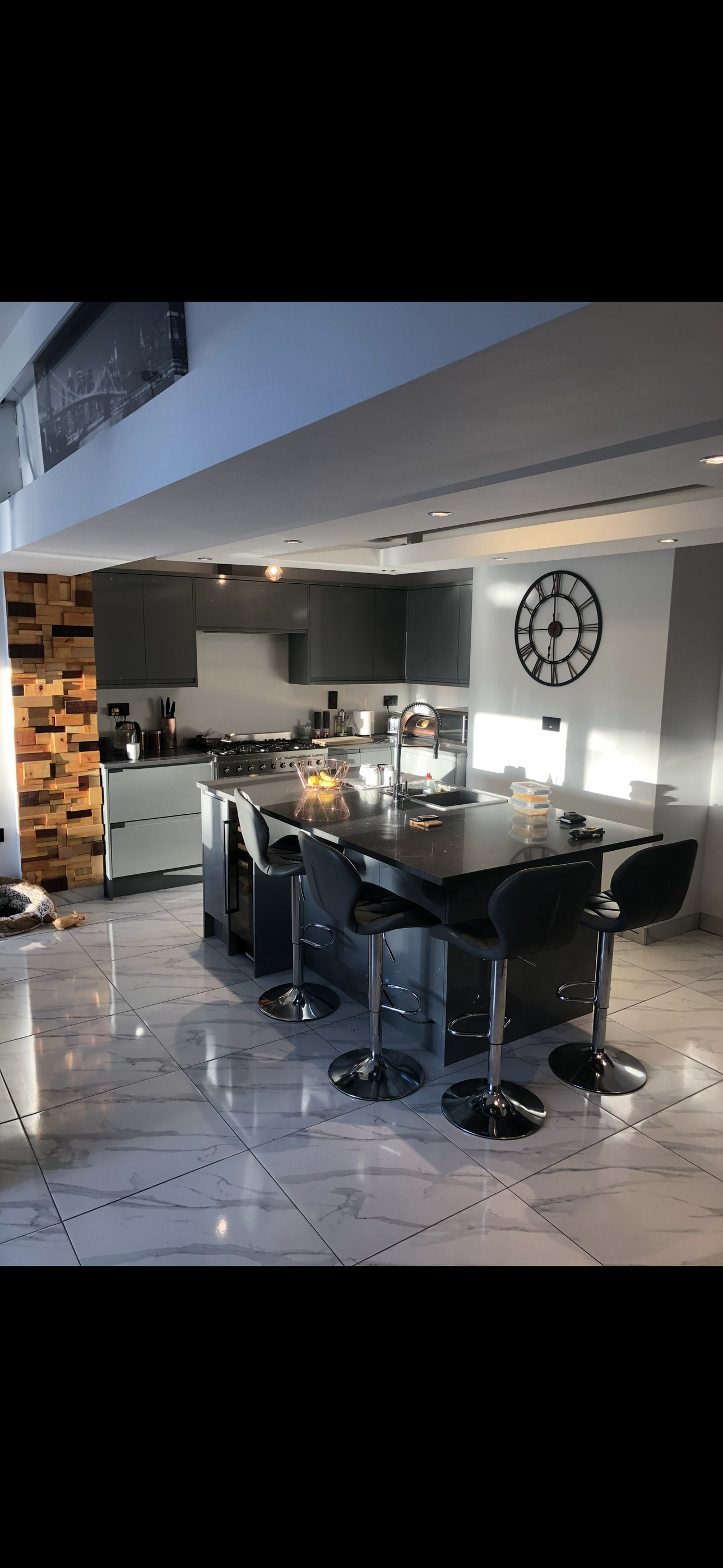 Dark grey handleless kitchen with large black granite island, bar stools and marble floor tiles