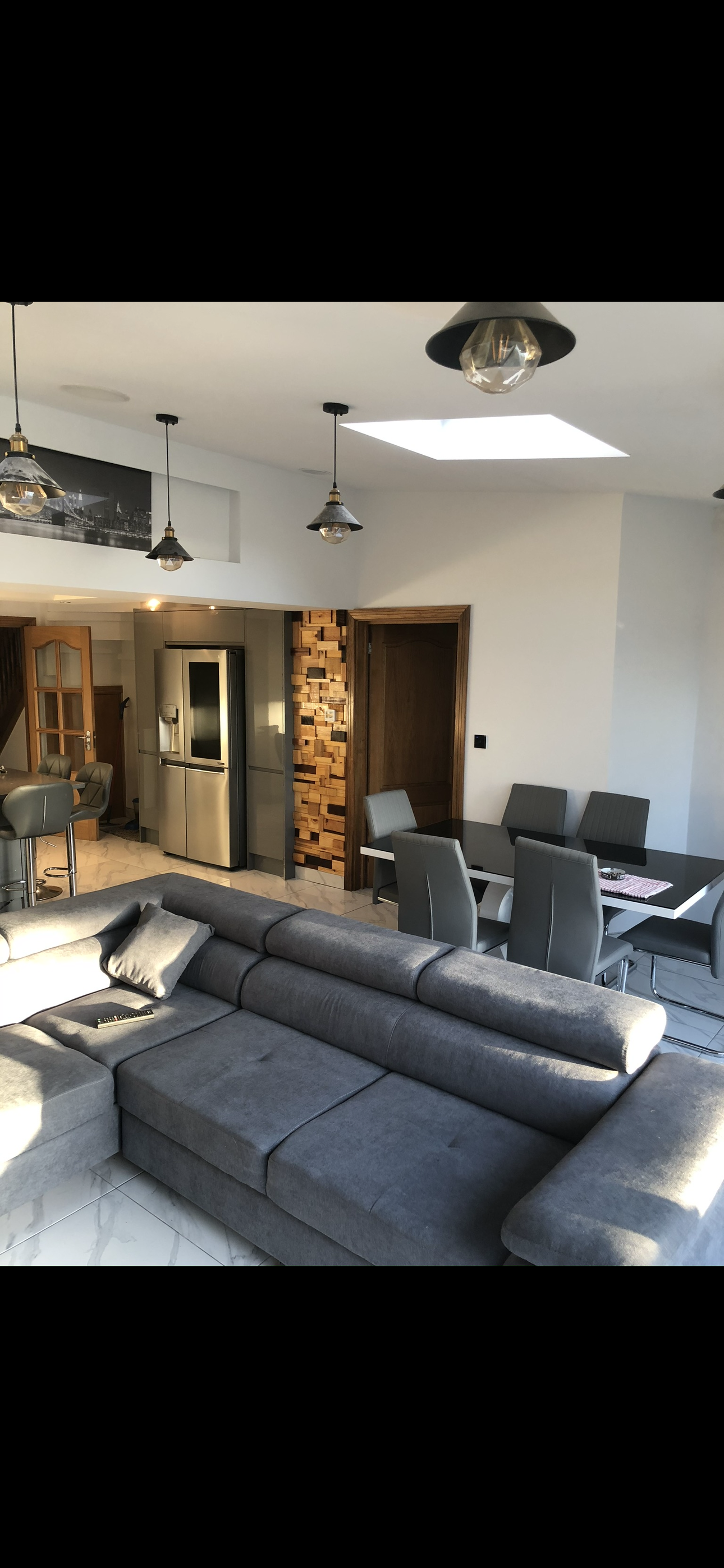 Open-plan dark grey kitchen and dining area with American fridge freezer, pendant lights and marble floor