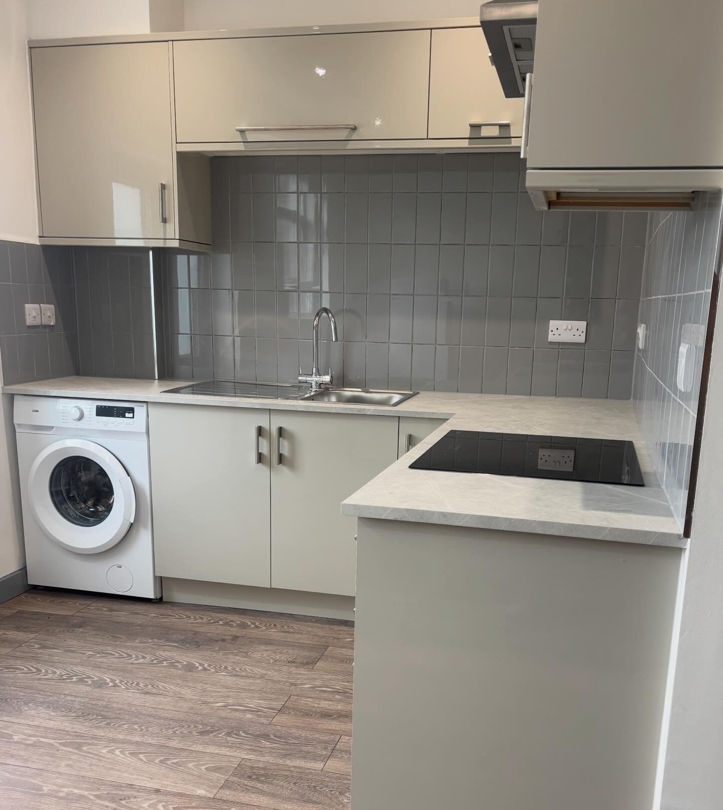 Cream gloss kitchen with grey square tile splashback, integrated washing machine and induction hob