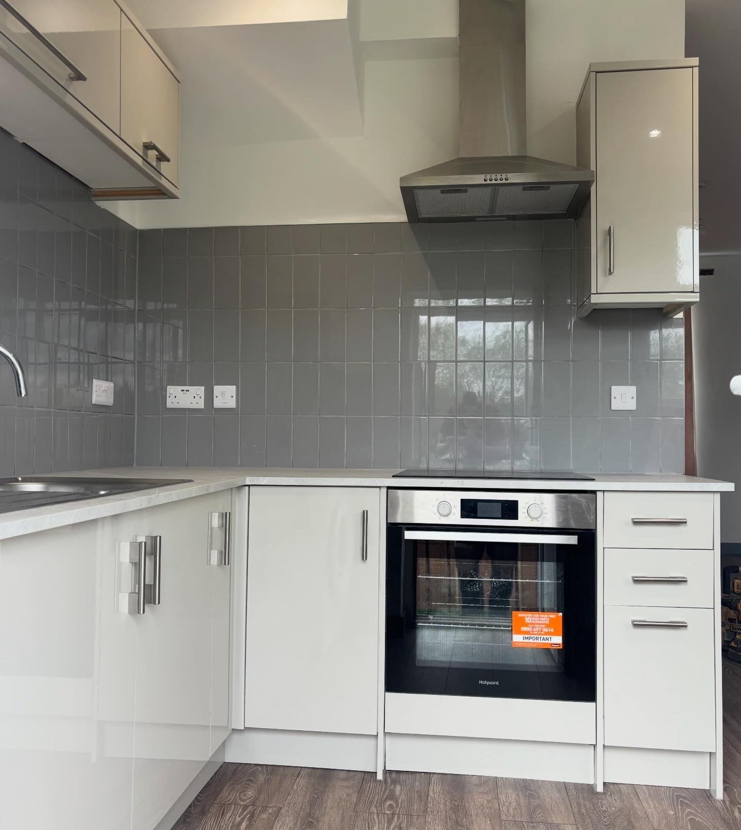 Cream gloss kitchen with grey square tile splashback, stainless steel oven and chimney extractor