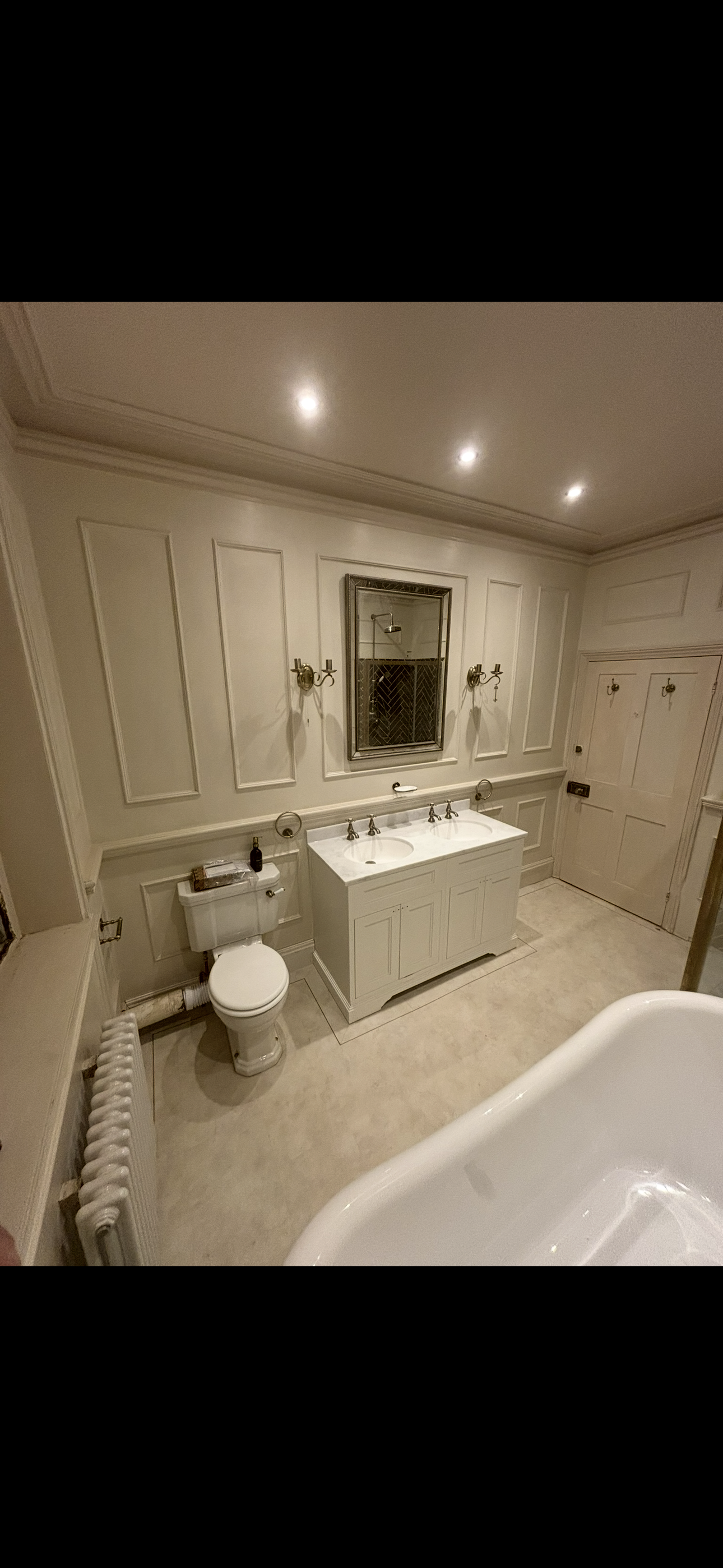 Classic cream bathroom with wall panelling, dual vanity unit, brass wall lights and freestanding bath