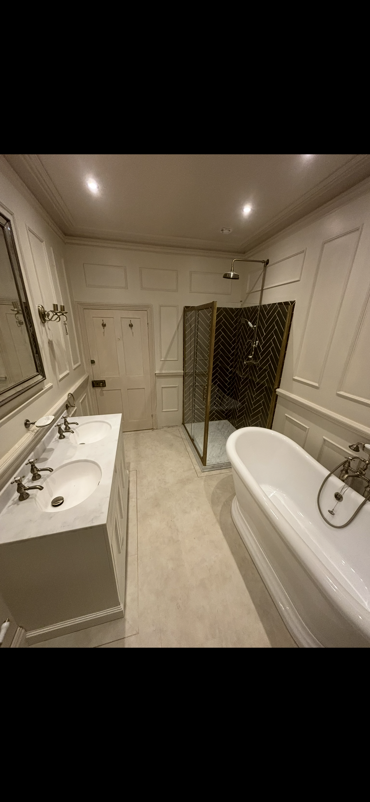 Classic cream bathroom with dual vanity, freestanding bath, brass herringbone shower enclosure and wall panelling