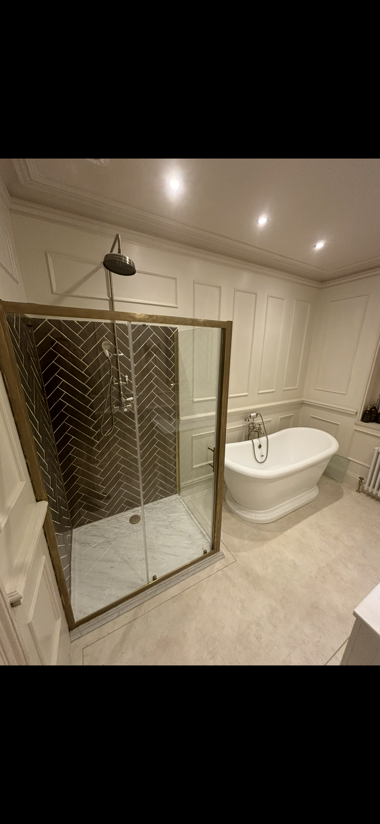 Classic cream bathroom with brass-framed herringbone shower enclosure, freestanding bath and wall panelling