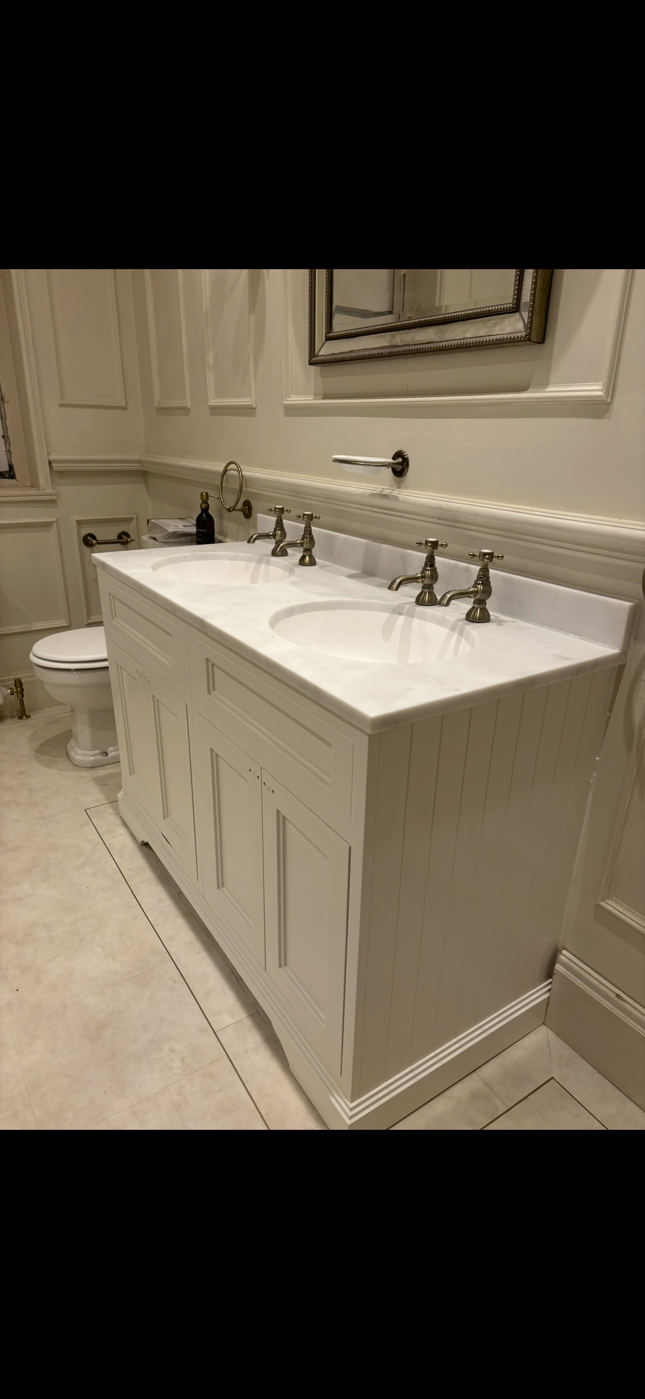 Close-up of classic white dual vanity unit with marble worktop, brass taps and ornate mirror