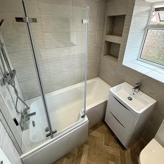 Beige tiled bathroom with bath and shower screen