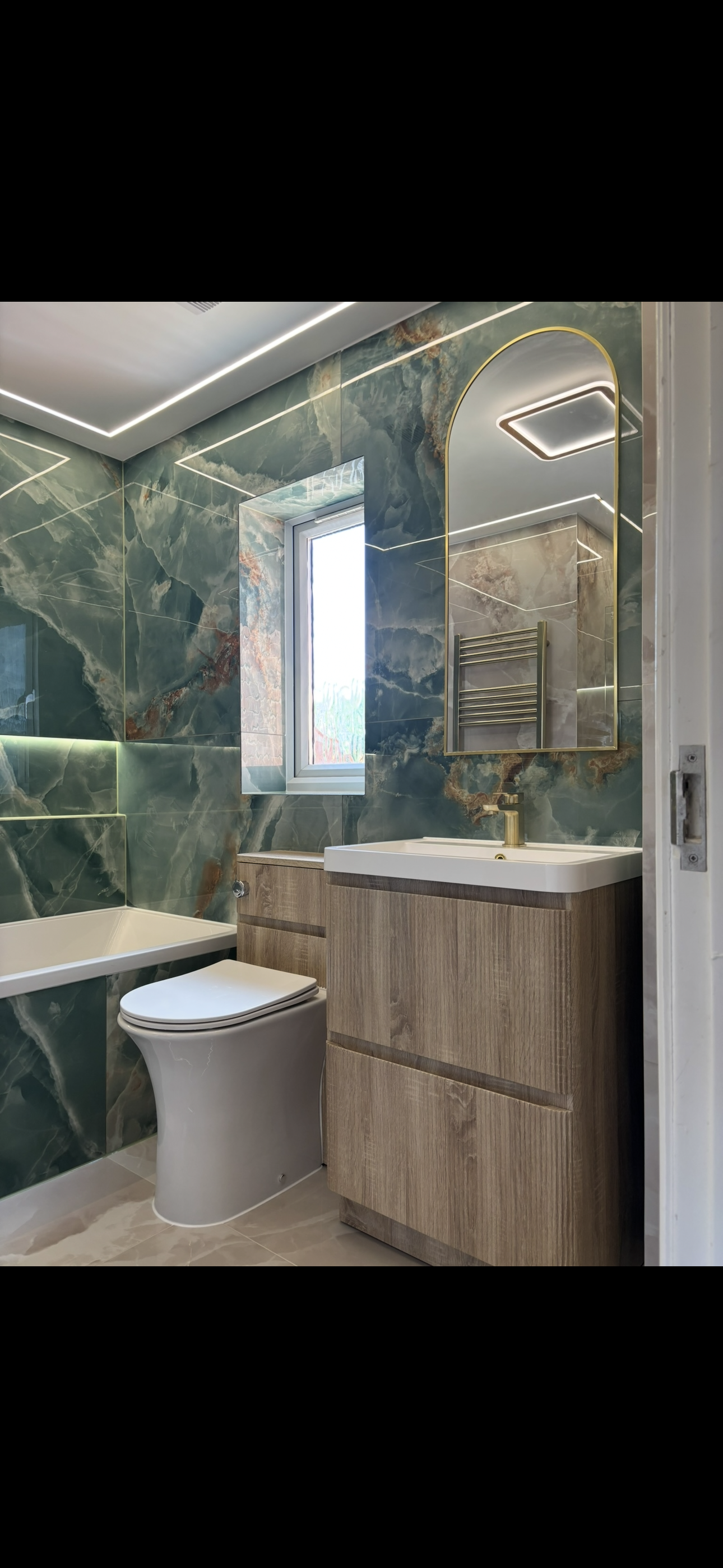 Green marble bathroom with arched gold mirror and wood vanity unit
