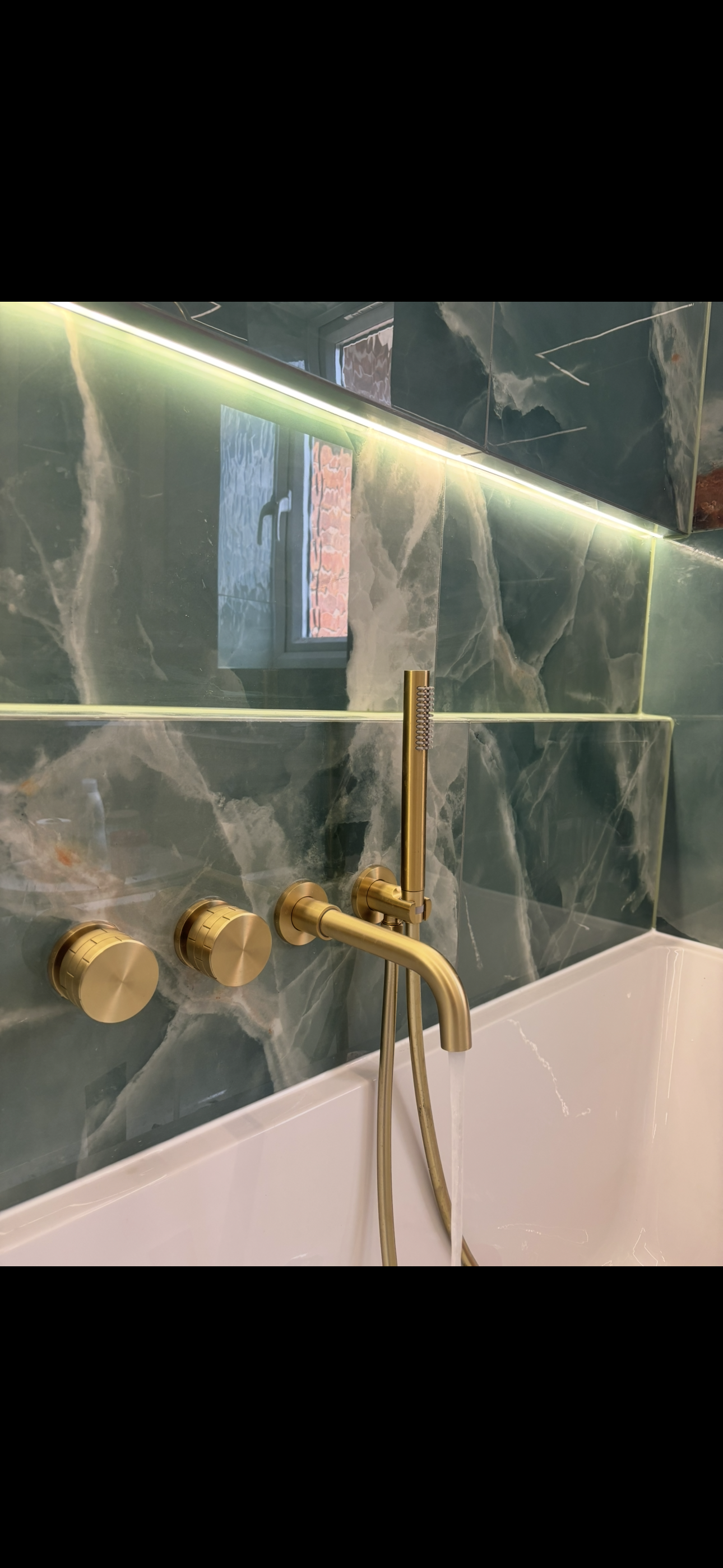 Brushed brass concealed bath taps and shower against green marble tiles